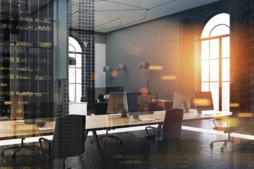 A modern office with long shared desks and tall arched windows at dusk